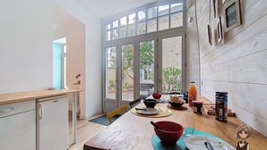Una cuina moderna amb taula de fusta, nevera i vista a un espai exterior per grans portes de vidre.