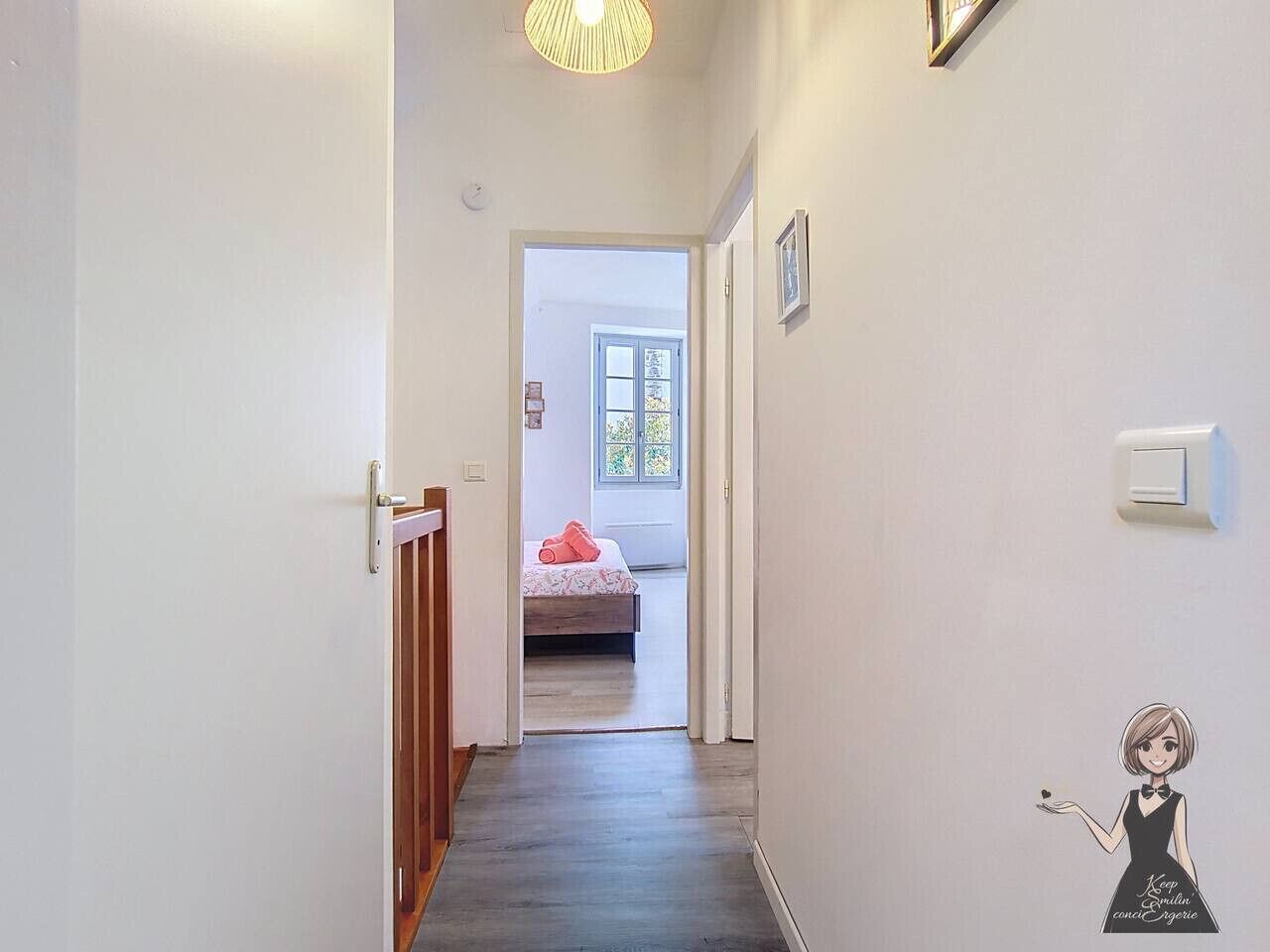 Een smalle gang die leidt naar een slaapkamer met een bed, een deur en een lamp.