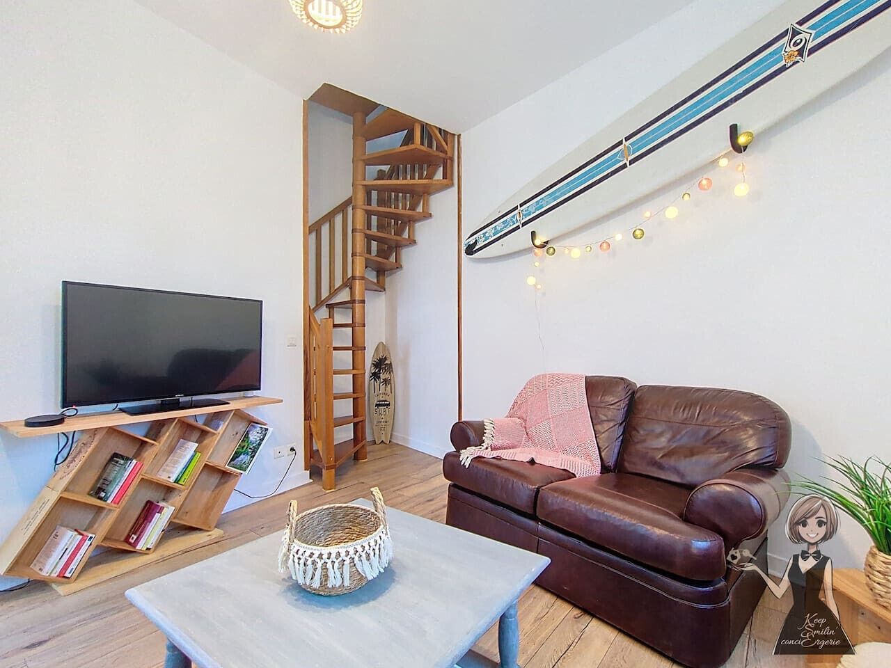 Un salon avec un canapé en cuir marron, un téléviseur à écran plat posé sur un meuble en bois, un escalier et une guirlande lumineuse accrochée au mur.