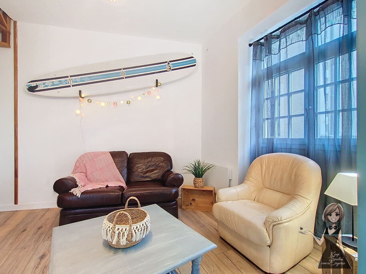 Een woonkamer met een bruine leren bank, een beige fauteuil, een houten salontafel en een surfplank aan de muur.
