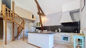 A modern kitchen with a central island, wooden staircase, and built-in appliances. - Gîte Cazette, un coin de Paradis au cœur du Béarn. (Ance Féas)