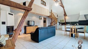 A spacious living area with a sofa, wooden dining table, and chairs. A staircase leads to an upper level. - Gîte Cazette, un coin de Paradis au cœur du Béarn. (Ance Féas)