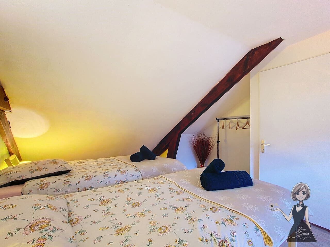 Ein Schlafzimmer mit schrägen Wänden, einem Bett mit floraler Bettwäsche, einem dunklen Holzbalken und einem Wandregal mit einem dekorativen Gegenstand.