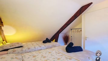 Ein Schlafzimmer mit schrägen Wänden, einem Bett mit floraler Bettwäsche, einem dunklen Holzbalken und einem Wandregal mit einem dekorativen Gegenstand.