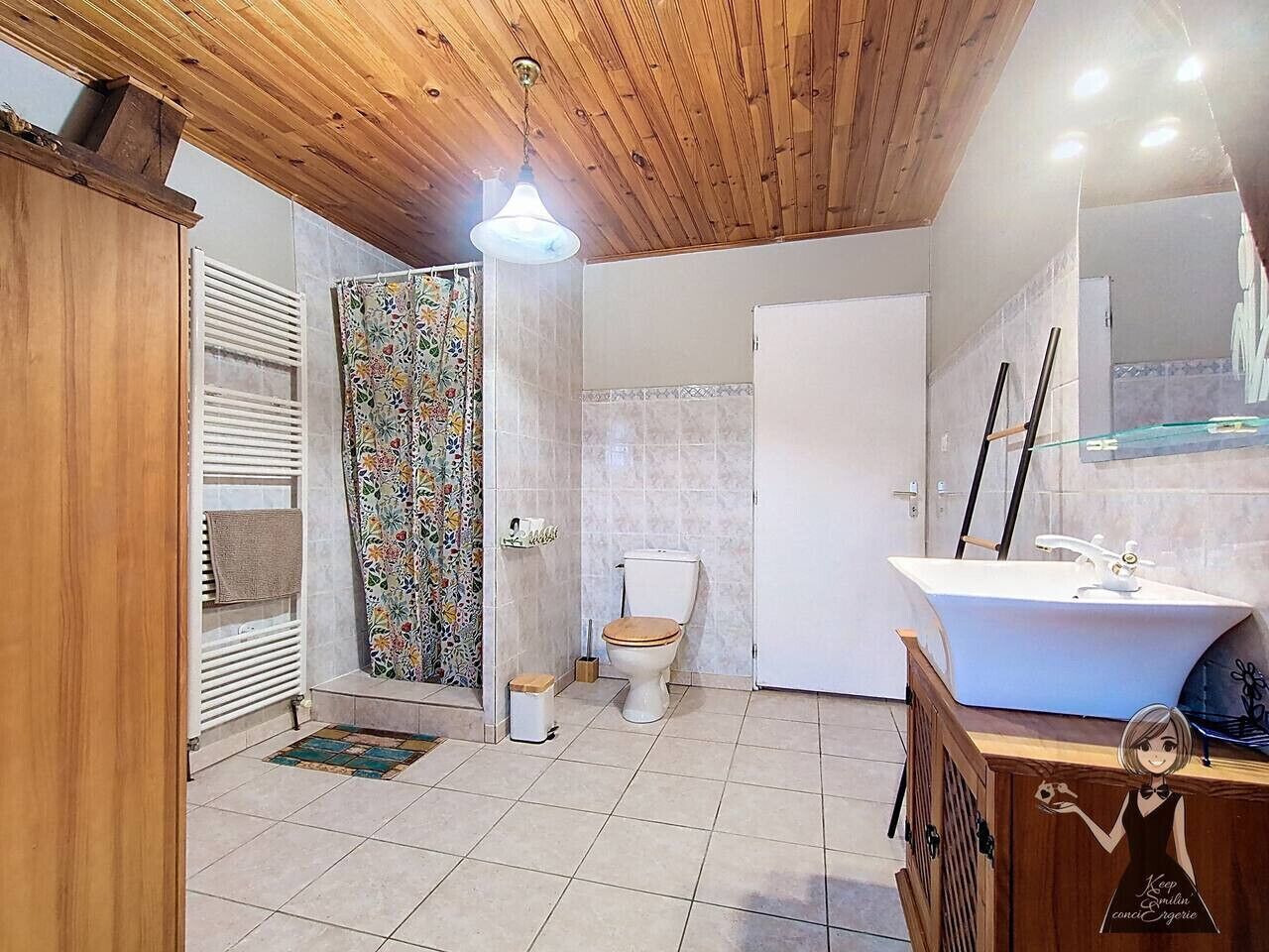 Een badkamer met een houten plafond, een wit toilet, een douche met een kleurrijk gordijn en een witte wastafel met een spiegel erboven.
