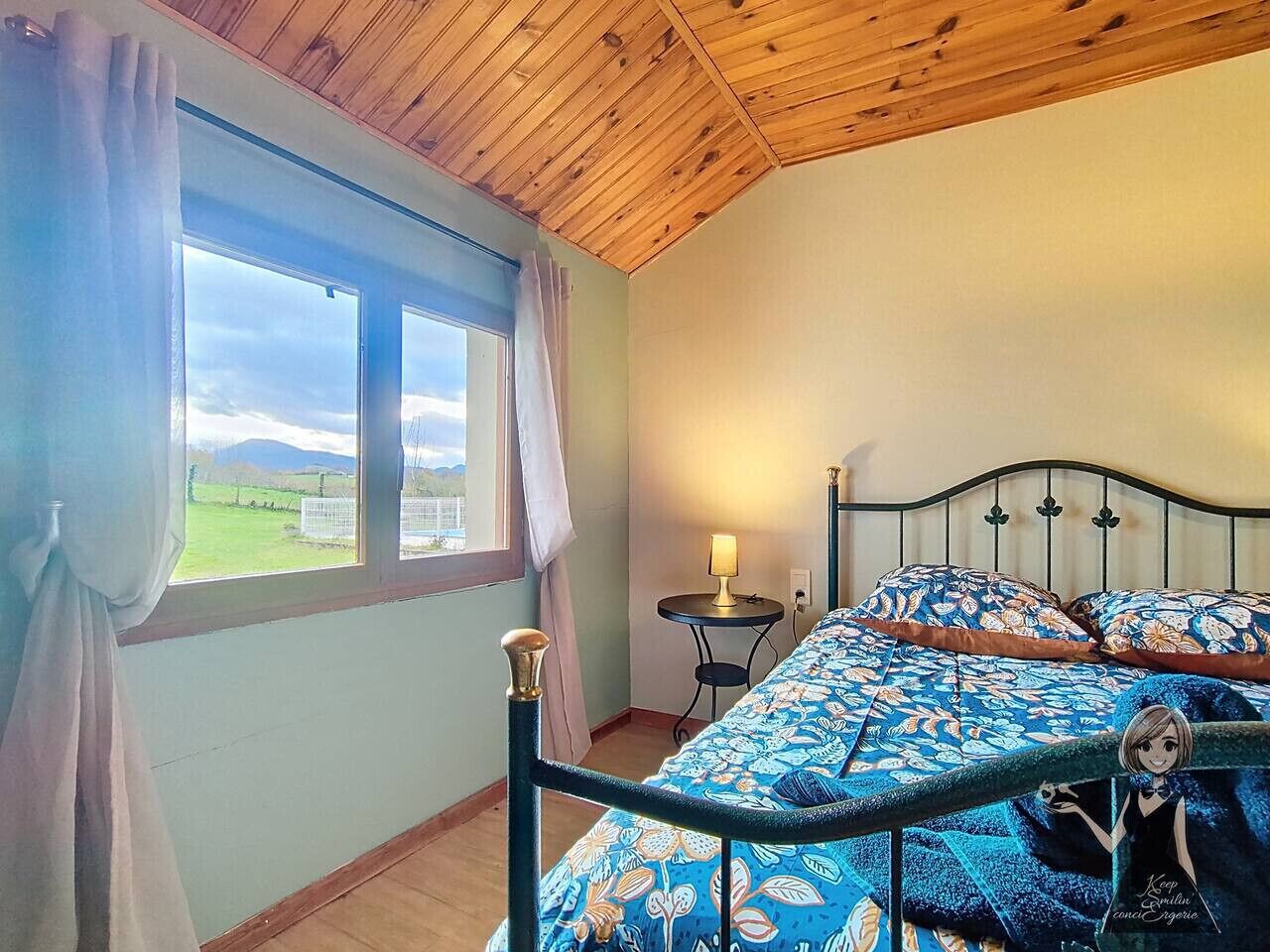 Ein Schlafzimmer mit Bett, Nachttisch, Lampe und Blick ins Freie durch ein Fenster.