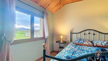Ein Schlafzimmer mit Bett, Nachttisch, Lampe und Blick ins Freie durch ein Fenster.