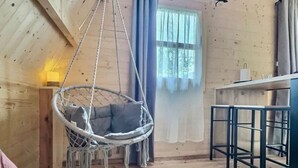 Een gezellig cabin interieur met een hangstoel, een barruimte en een groot raam met gordijnen.
