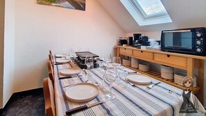 A dining area with a table set for six, a microwave, and a shelf with dishes. - Le Refuge, Cocon pour 8 avec Spa & Piscine chauf. (Cauterets)