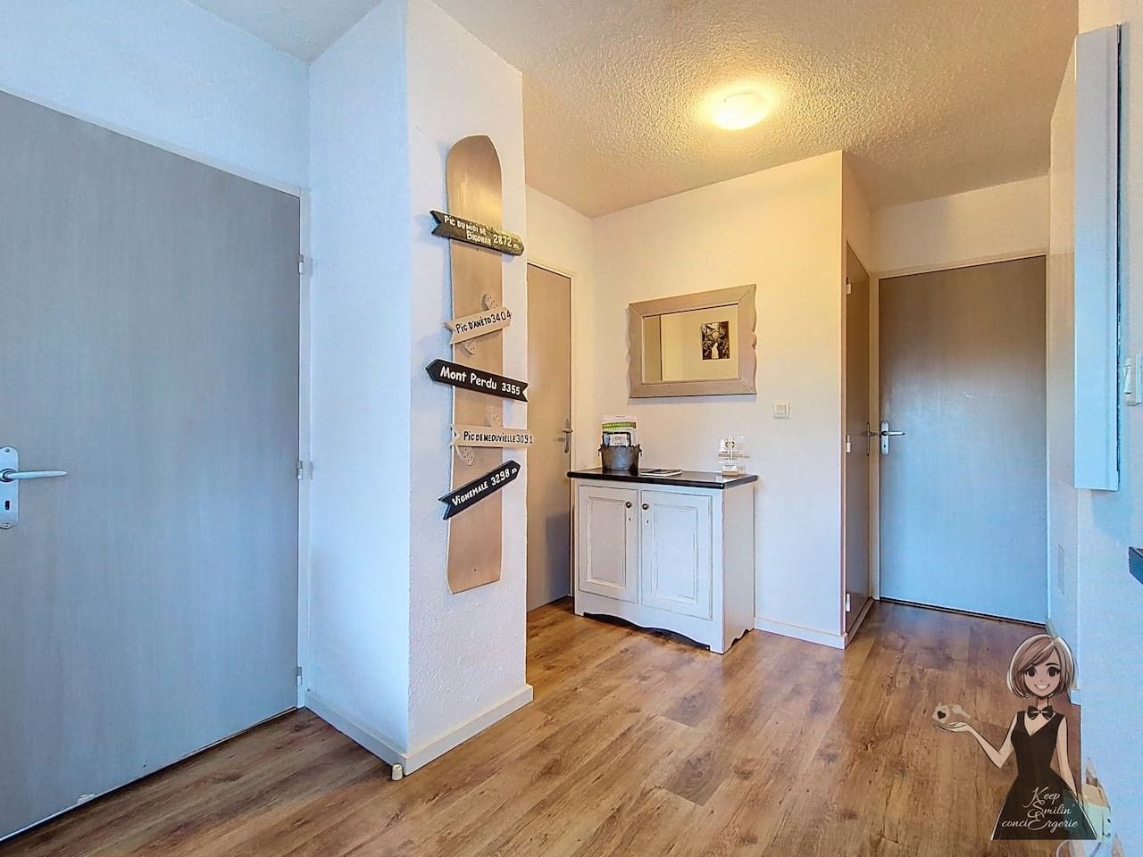 Un couloir doté d’un plancher en bois, de murs blancs et d’une armoire dans laquelle est encadrée une image.