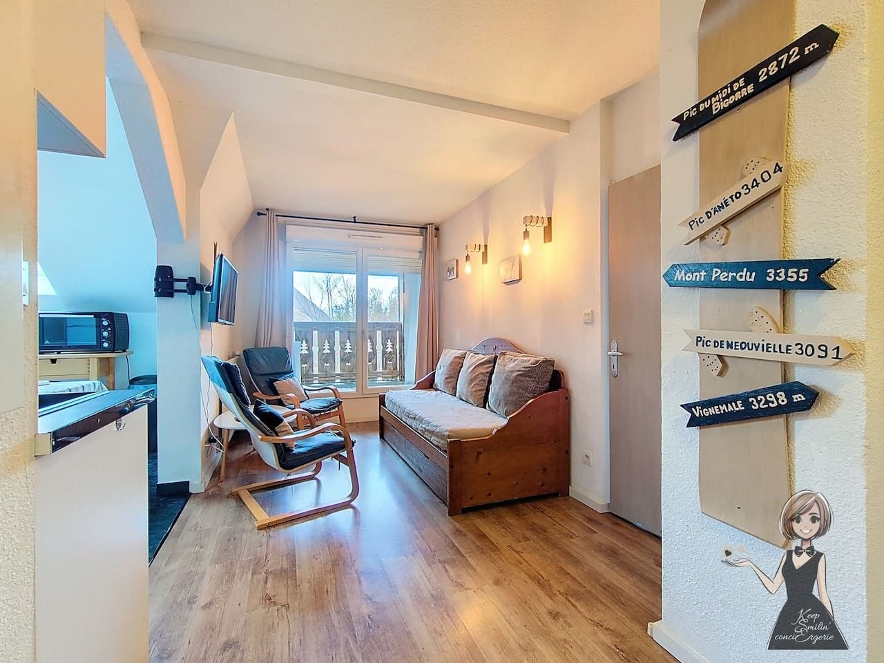 Un salon confortable avec un canapé, un fauteuil et un téléviseur. Des lampes sont fixées au mur et il y a une fenêtre avec des rideaux.