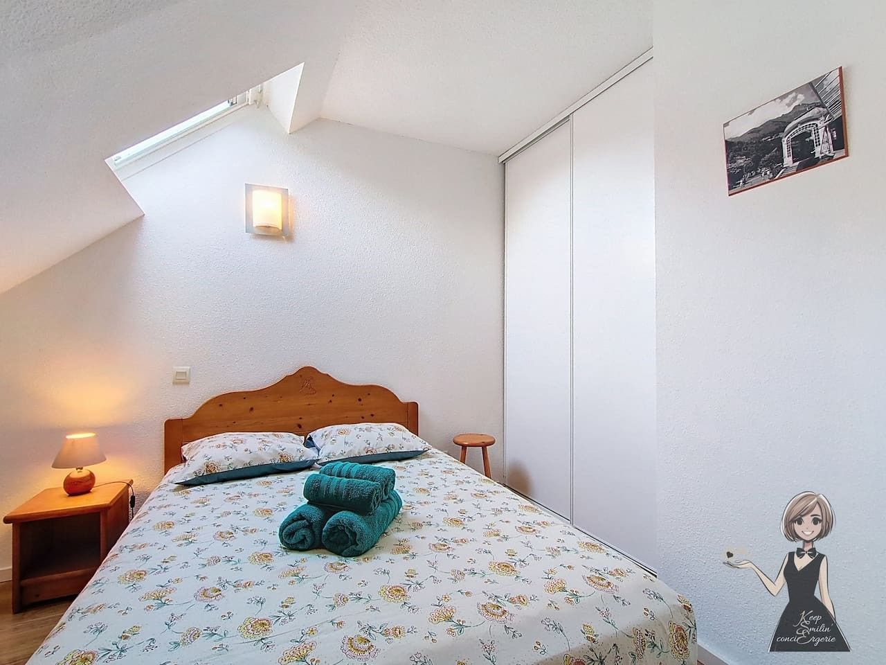 Une chambre à coucher comprenant un lit, une table de chevet, une lampe, un luminaire fixé au mur et un tableau encadré.