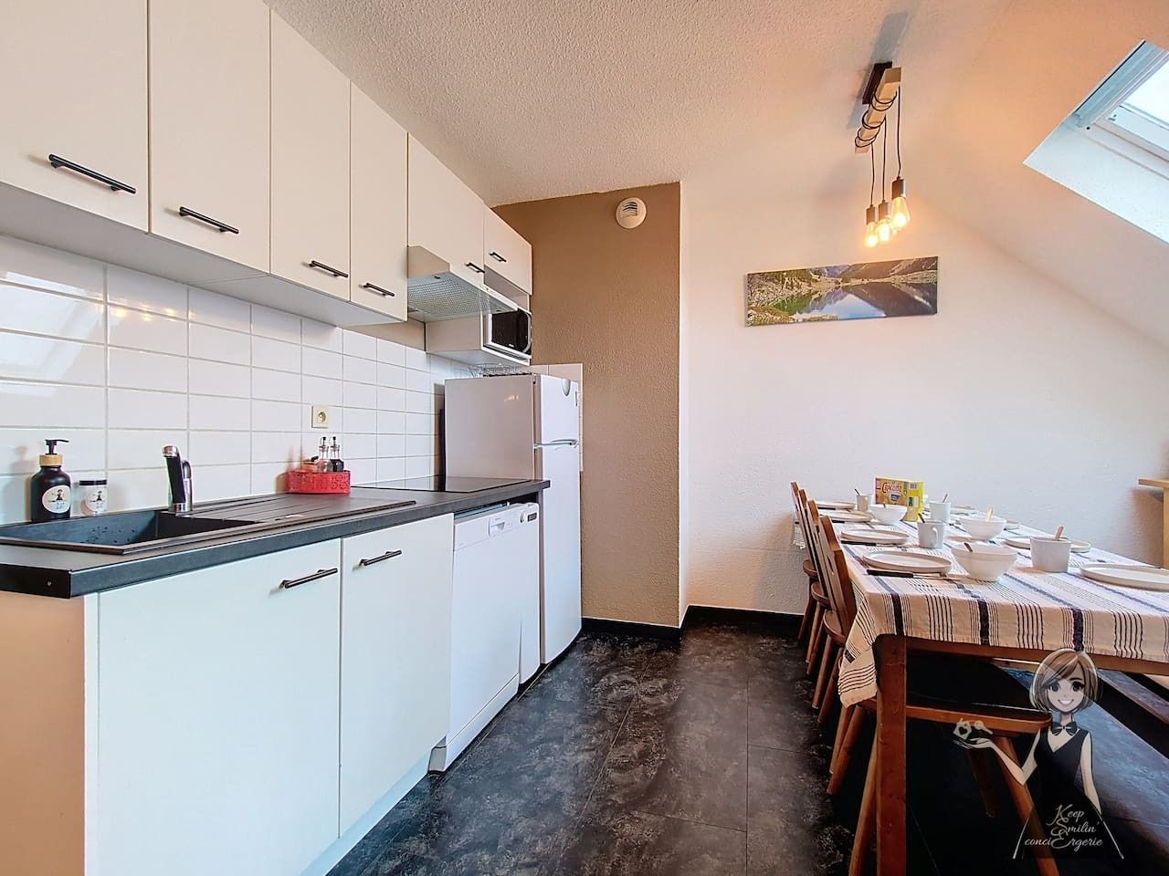 Una cocina moderna con armarios blancos, encimera negra y un comedor con mesa para dos.