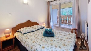 A bedroom with a bed, bedside lamps, a window with curtains, and a view of trees outside. - Le Refuge, Cocon pour 8 avec Spa & Piscine chauf. (Cauterets)