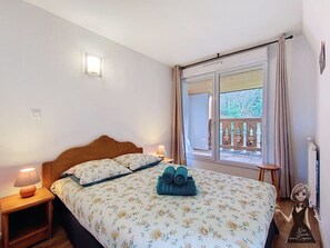 Quarto com cama, abajures, janela com cortinas e vista para árvores.
