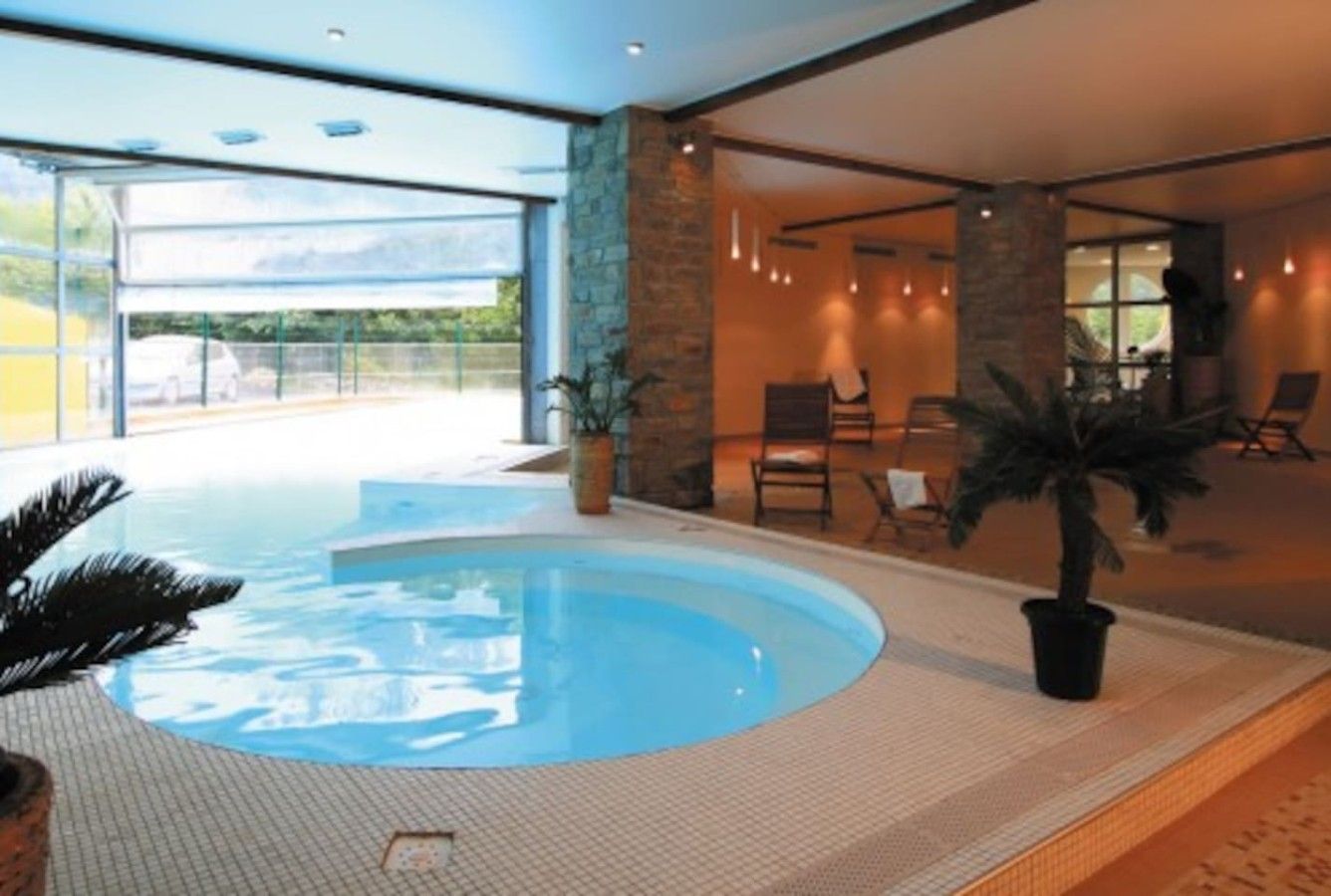 Una piscina interior con suelo de baldosas, rodeada de un área de descanso con sillones y una planta en maceta.