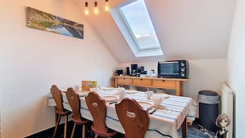 A dining area with a table set for four, a microwave, and a trash bin.