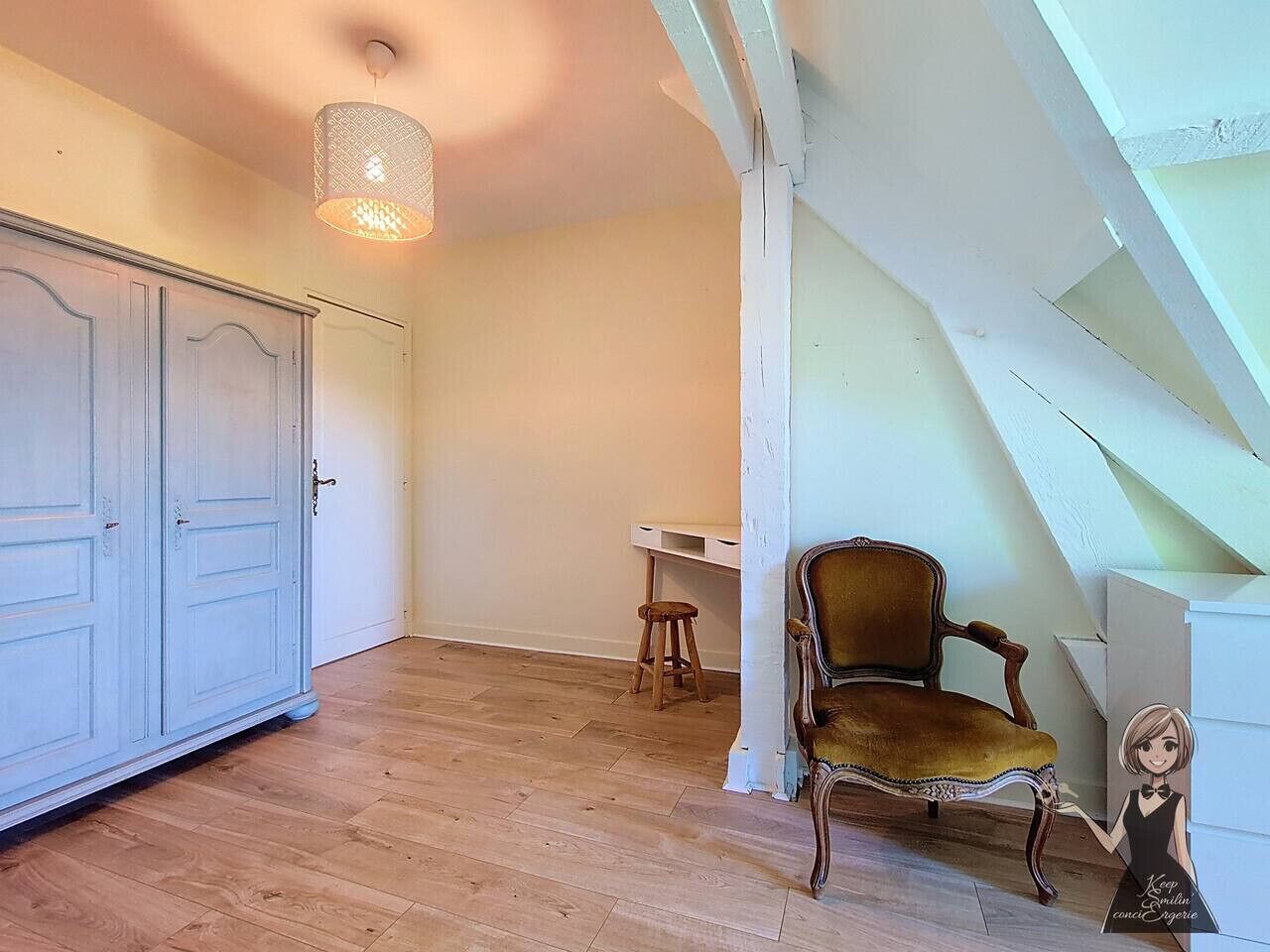 Et værelse med trægulv, et hvidt klædeskab, en træstol, en lille skammel og en hængende lampe.