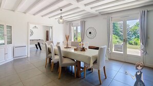 Uma sala de jantar com mesa e cadeiras brancas, um candelabro e vista para o verde lá fora.