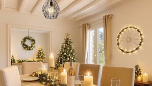 Uma sala de jantar com mesa posta para quatro pessoas, com velas, árvore de Natal e decoração festiva.