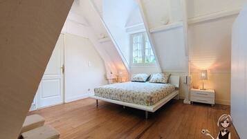A bedroom with a sloped ceiling, a bed with floral bedding, a nightstand, and a lamp.