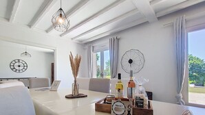 Quarto de hotel com cama branca, uma mesa de jantar com bandeja de comida, garrafas de vinho e um relógio decorativo.