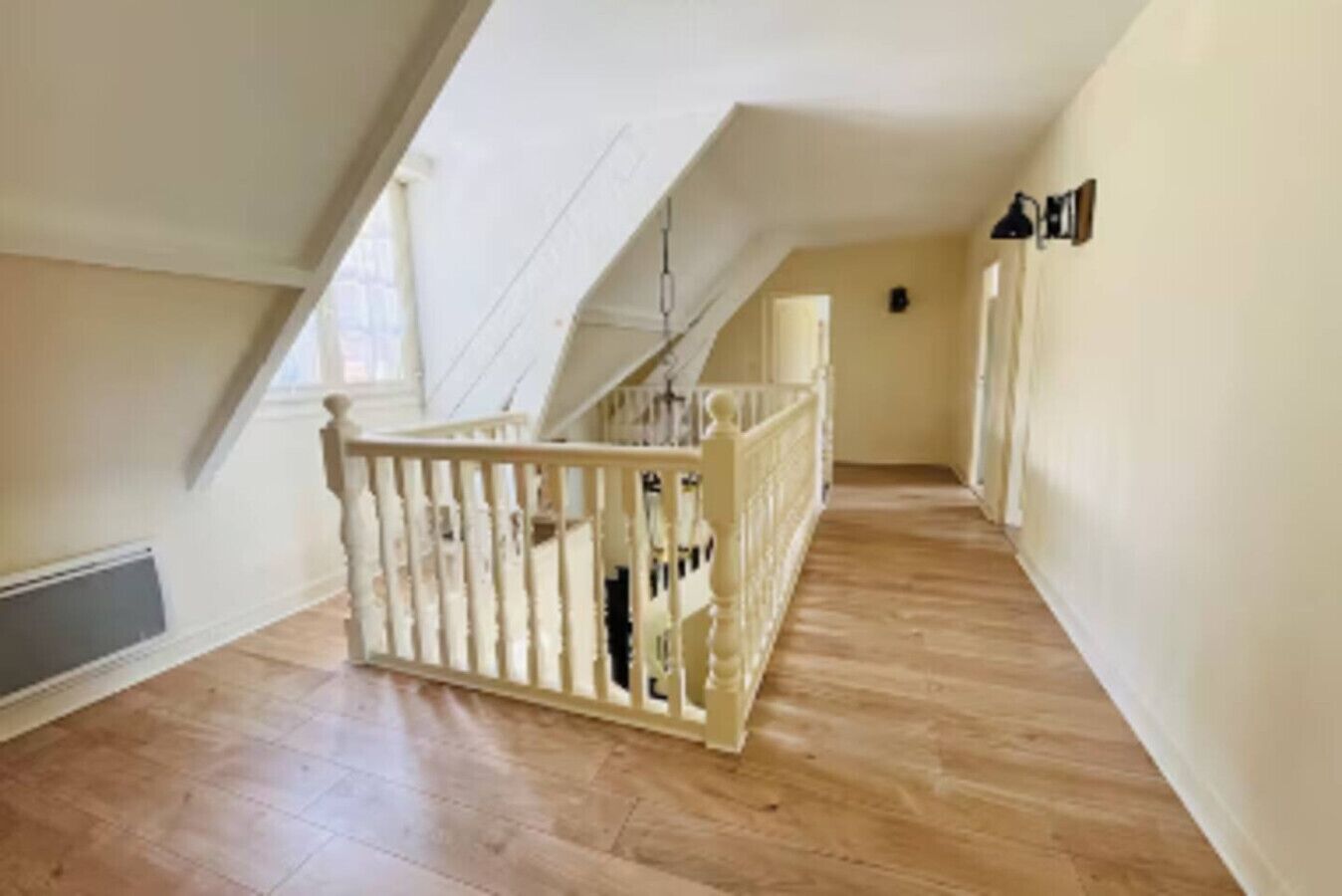 A spacious attic room with a wooden floor, a white railing, and a sloped ceiling.