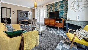 Ett vardagsrum med ett rutmönstrat golv, en gul soffa, ett träskåp, en tv och en öppen spis.