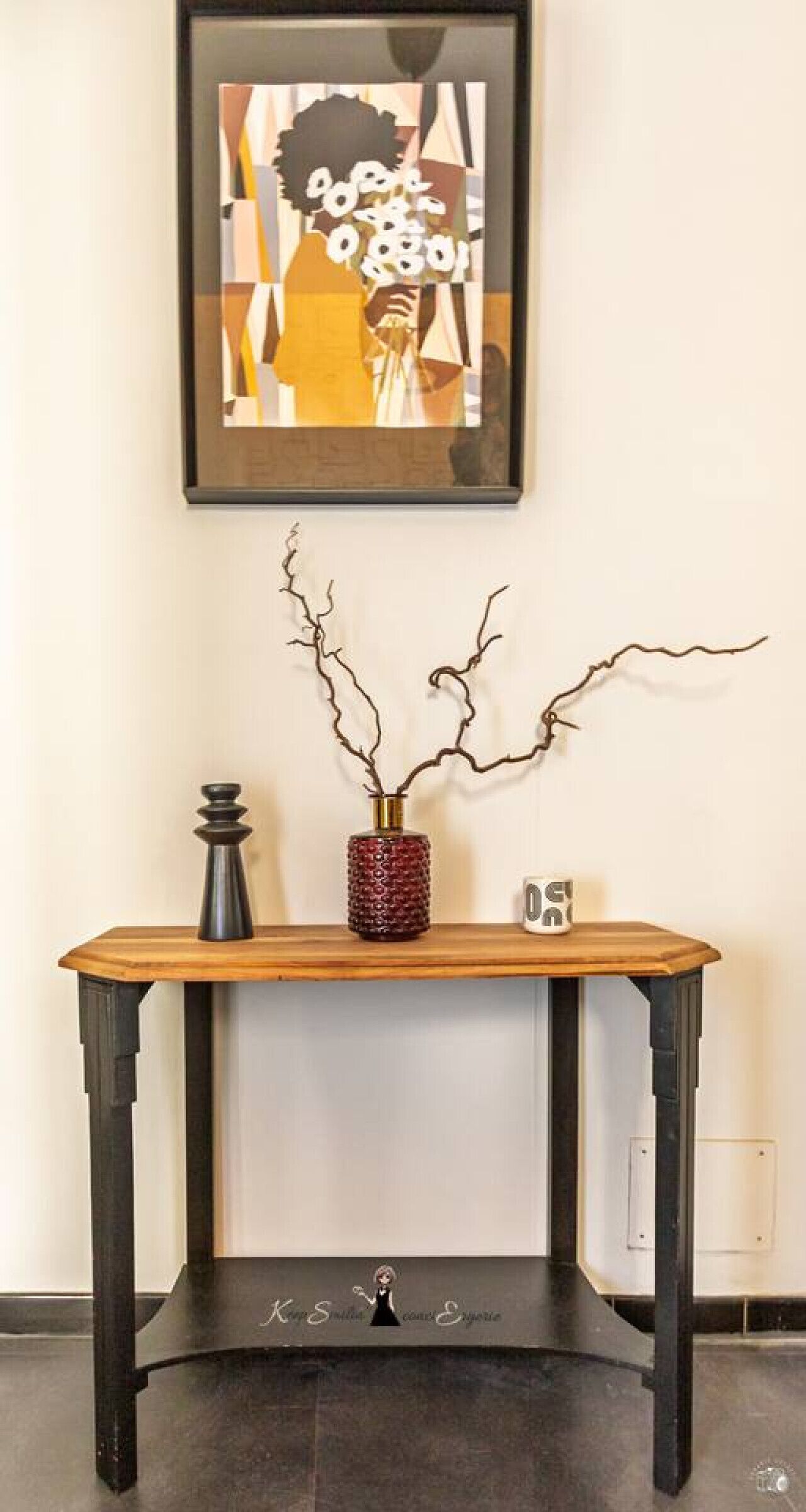 A wooden console table with a vase of branches, a decorative object, and a mug.