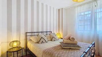 Una cama bien hecha con almohadones estampados, una lámpara de noche y una toalla enrollada sobre la mesita de noche.