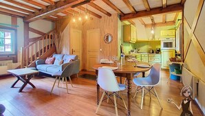 Ein gemütlicher Raum mit Holzbalkendecke, einem Esstisch mit Stühlen, einer Couch und einer Treppe, die in einen anderen Raum führt.