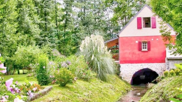 Ein rotes und weißes Haus mit einem kleinen Tunnel-Eingang, umgeben von üppigem Grün und blühenden Pflanzen.