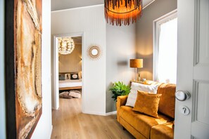 A modern living room with a wooden floor, a mustard-colored sofa, a hanging light fixture, and a door with a keyhole. - 10 Floor Apartments (Como)