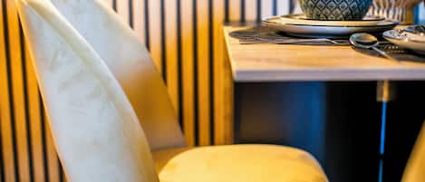 A chair with a white backrest and yellow cushion, a table with a blue patterned bowl and a spoon, and vertical blinds in the background.