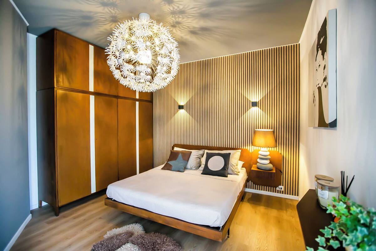 A modern bedroom with a wooden bed, a hanging light fixture, and a wall-mounted lamp.