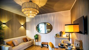 A modern living room with a sofa, a dining table with chairs, a chandelier, a mirror, and a Buddha statue. - 10 Floor Apartments (Como)