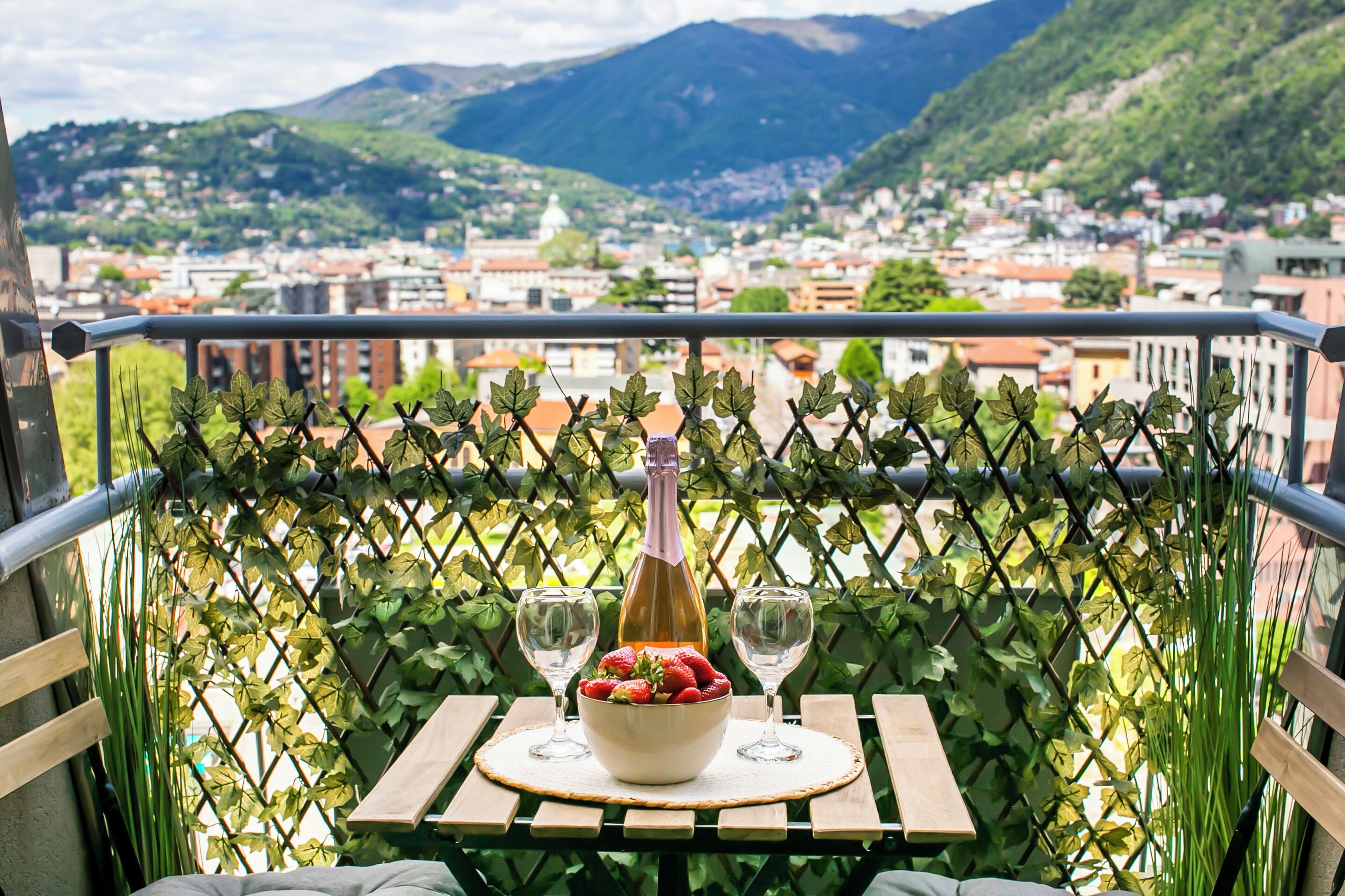 A balcony with a table set for two, a bottle of wine, and a bowl of strawberries.