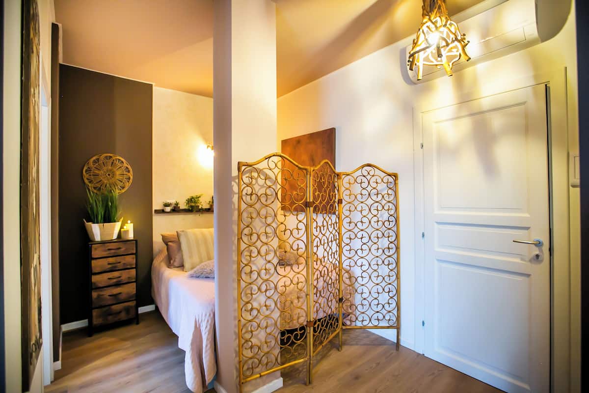 A bedroom with a bed, a decorative screen, a wooden dresser, and a white door.