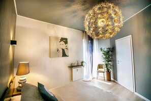 A modern bedroom with a bed, a bedside lamp, a wall-mounted artwork, a radiator, a potted plant, and a door. - 10 Floor Apartments (Como)
