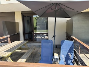 Eine Terrasse mit einer Holzbank, einem blauen Stuhl, einem Sonnenschirm und Blick auf eine grüne Landschaft.