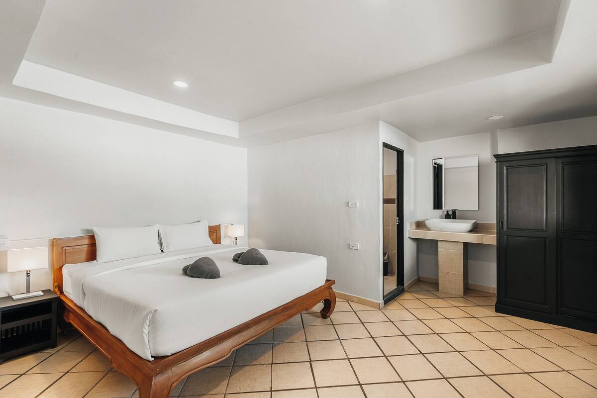 A bedroom with a wooden bed, a bedside table, a nightstand, a bathroom with a sink and mirror.