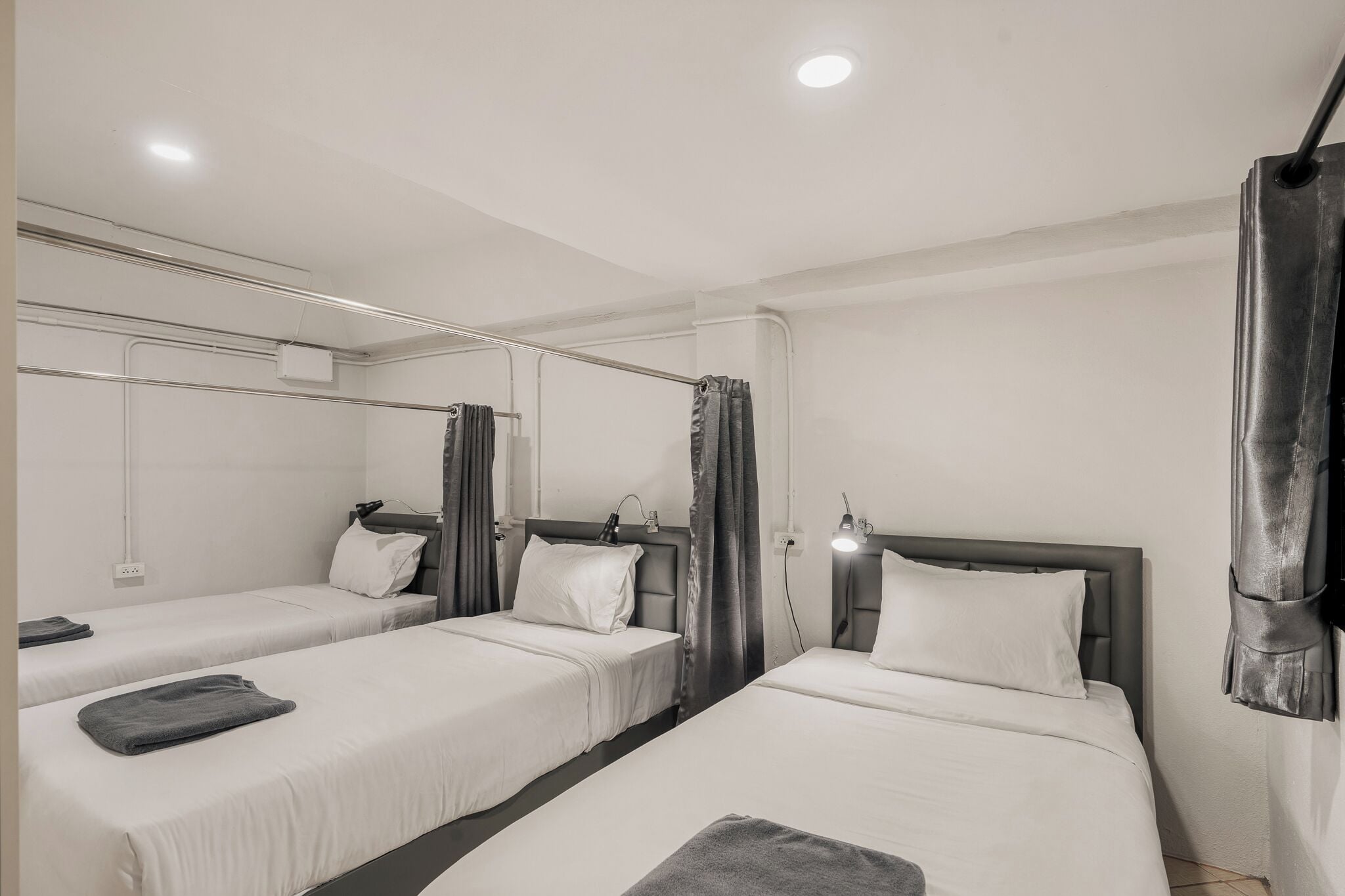 A hotel room with three single beds, a large mirror, and a modern design.