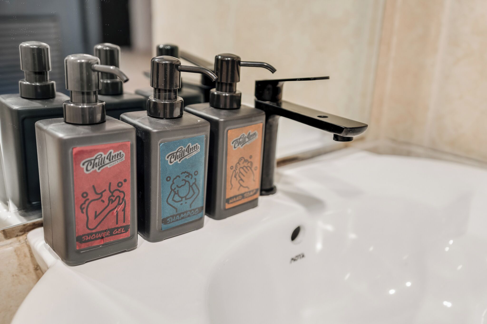 Une salle de bain avec un lavabo blanc, trois distributeurs de savon étiquetés « Chiquita », « Philippine » et « Philippine », et une douchette à main.