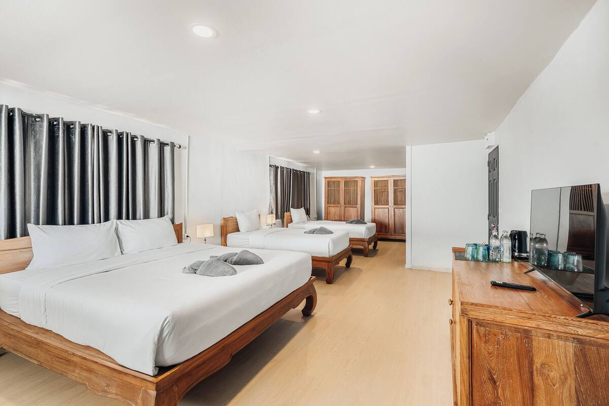 A hotel room with a large bed, two smaller beds, a wooden dresser, and a television.