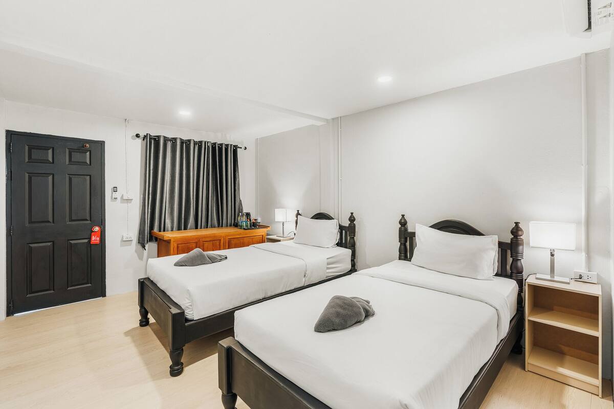 A hotel room with two beds, a wooden dresser, a desk with a lamp, and a black door.