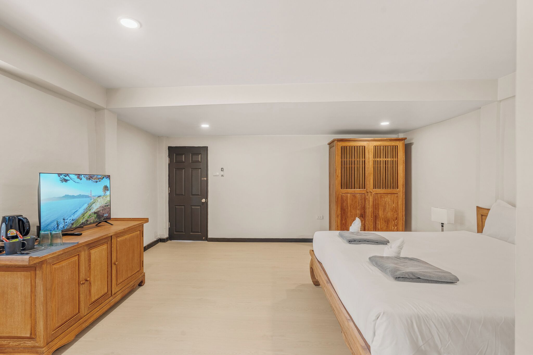A bedroom with a bed, a wooden wardrobe, a television, and a door.