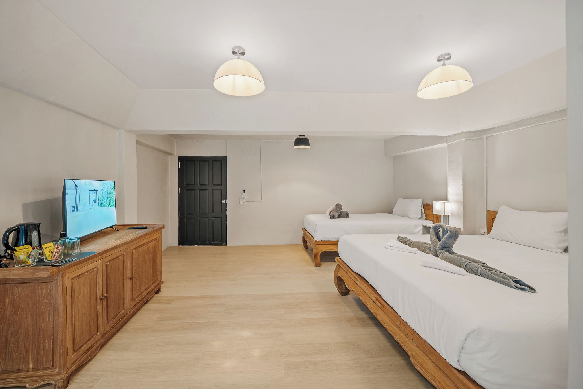 Habitación de hotel con dos camas, un aparador de madera, un televisor y una puerta.