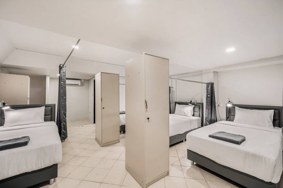 A hotel room with three beds, a wardrobe, and a ceiling light.