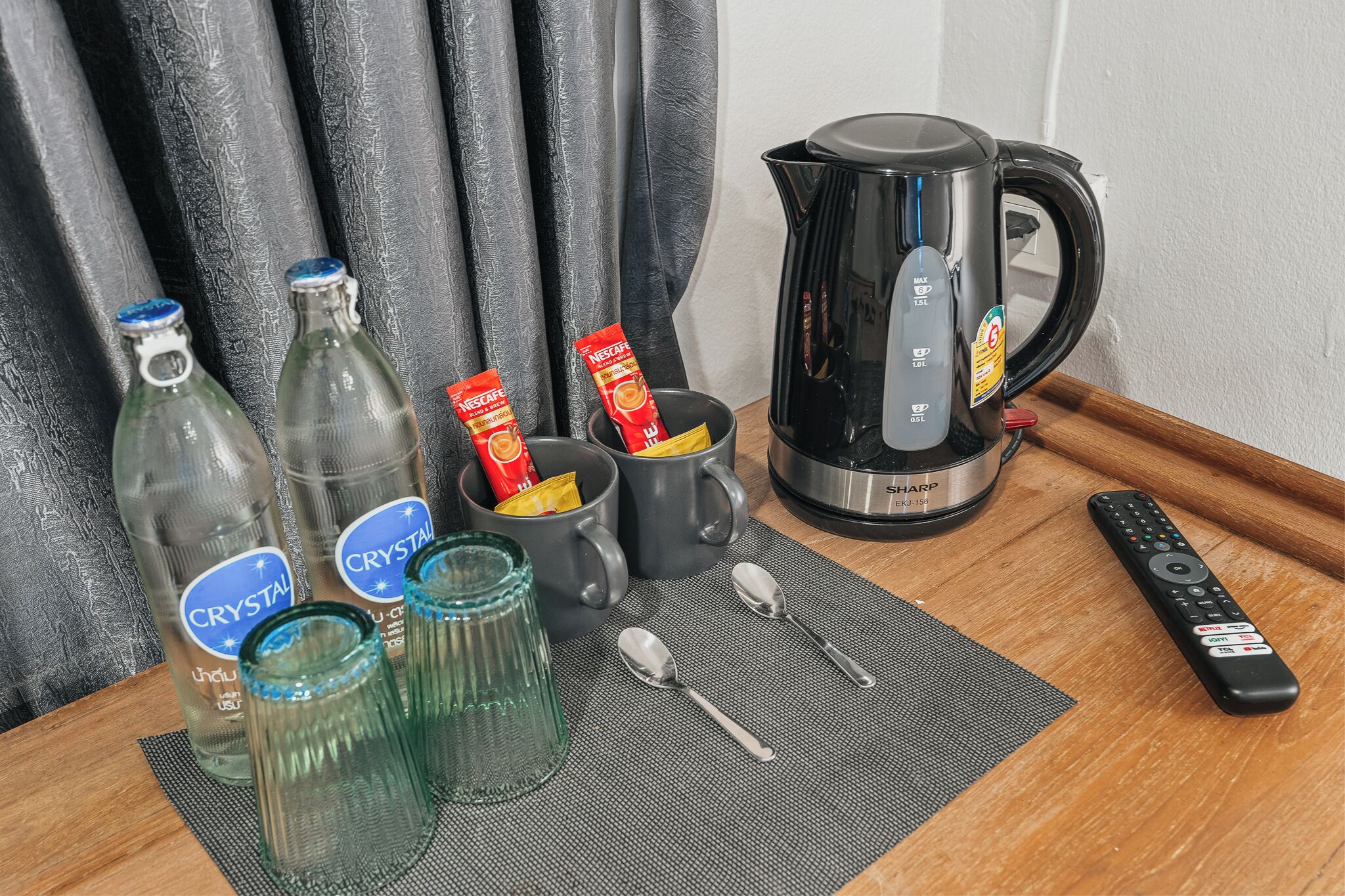 A table with bottles, glasses, a kettle, and a remote control.