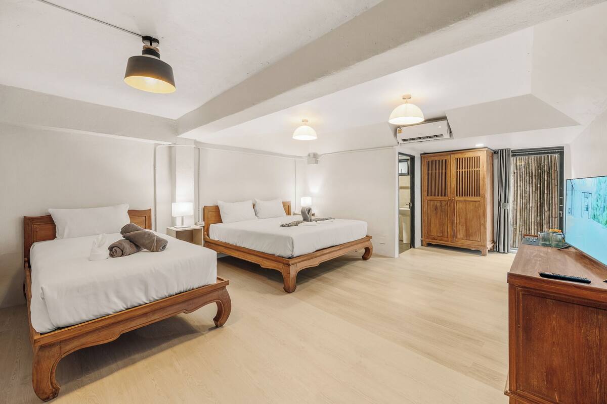 A hotel room with two wooden beds, a wooden cabinet, a television, and a ceiling light fixture.